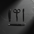 Flat lay of men's eyebrow grooming kit with scissors, spoolie brush, razor and tweezers on dark slate background